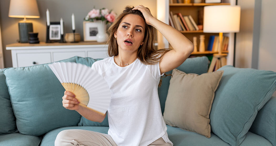 Woman puts head on sofa cushions feels sluggish due unbearable heat, waves hand fan cool herself, hot summer flat without air-conditioner climate control system concept